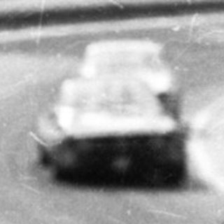 Classic race car on oval track with spectators watching.