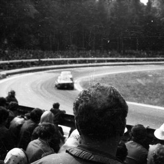 Classic race car on oval track with spectators watching.