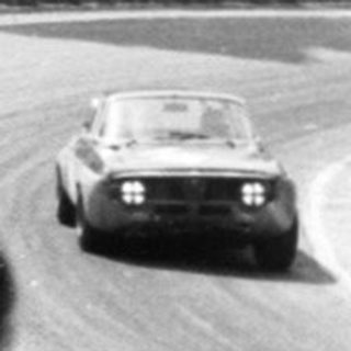 Classic car race on oval track with spectators.
