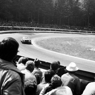 Classic car race on oval track with spectators.