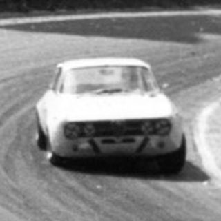 Classic race car on curved track with spectators.