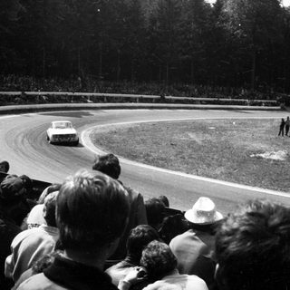 Classic race car on curved track with spectators.