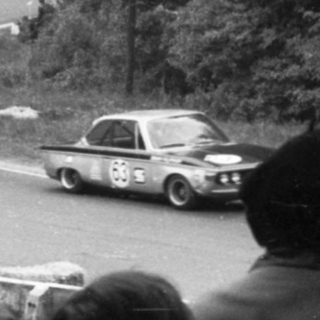 Historic rally cars racing on winding forest road.