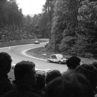 Historic rally cars racing on winding forest road.