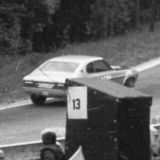 Rally car racing on winding mountain road with spectators.