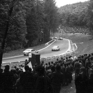 Rally car racing on winding mountain road with spectators.