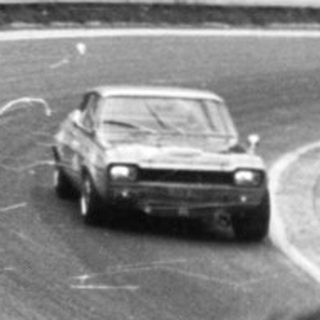 Classic race car on wet track during rally.