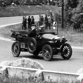 Vintage race car driving on winding road with spectators.