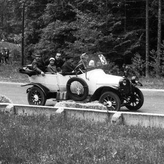 Vintage race car on rural road with spectators.