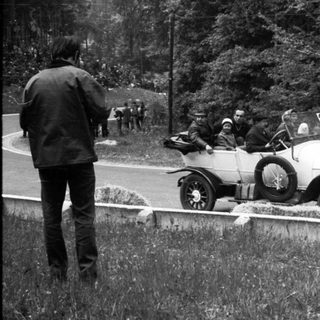 Vintage race car on rural road with spectators.