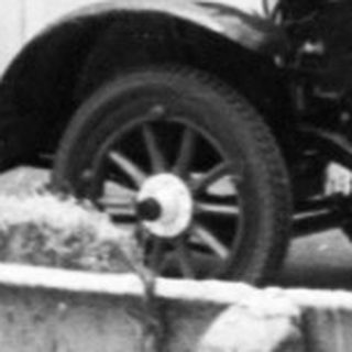 Vintage race car on rural road with spectators.