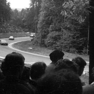 Race car driving on winding road with spectators watching.