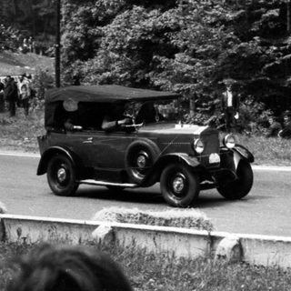 Classic car race on rural road with spectators.