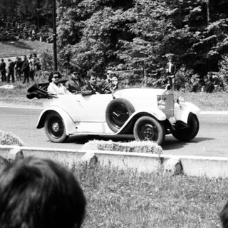 Classic race car driving on road with spectators.