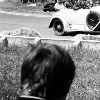 Classic race car driving on road with spectators.