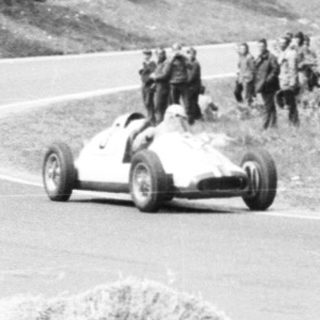 Classic race car on curving road during vintage rally.