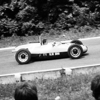 Classic race car on curvy road with spectators watching.