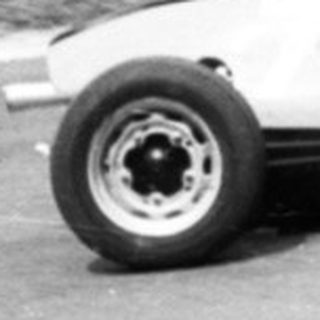 Classic race car on curvy road with spectators watching.