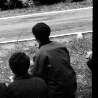 Classic race car on curvy road with spectators watching.