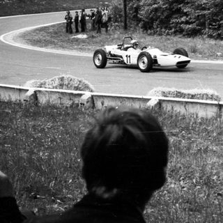 Classic race car on curved roadway during vintage motorsport event.