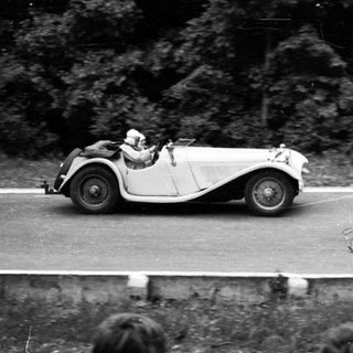 Classic race car driving on winding road.