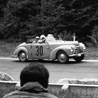 Classic race car driving on road during rally.
