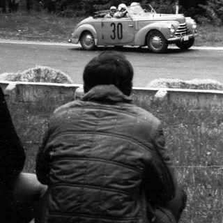 Classic race car driving on road during rally.