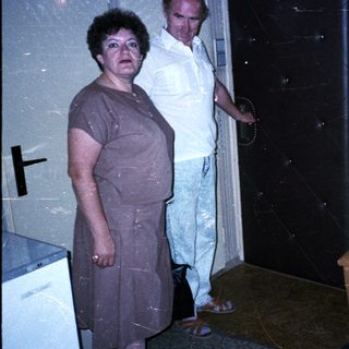 Three people in a dimly lit room, one sitting, others standing.