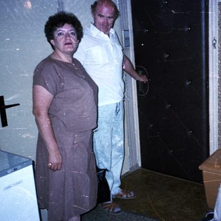 Three people in a dimly lit room, one sitting, others standing.