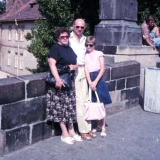Family posing near historic statue on bridge.