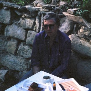 Two men sitting outdoors near stone wall.