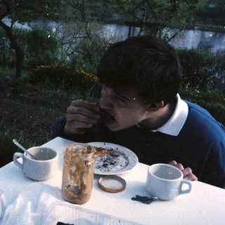 Man eating cake outdoors by a table.