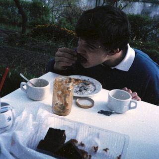 Man eating cake outdoors by a table.
