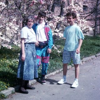 Three people posing by blooming cherry blossom tree.