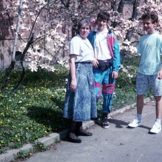 Three people posing by blooming cherry blossom tree.
