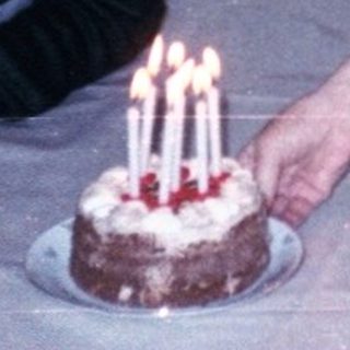 A woman lighting candles on two birthday cakes with a young boy seated.