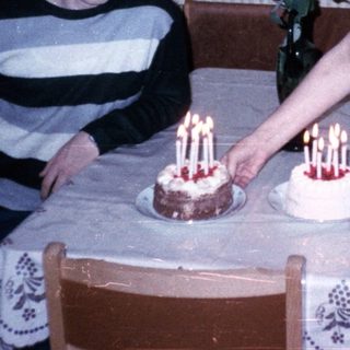 A woman lighting candles on two birthday cakes with a young boy seated.