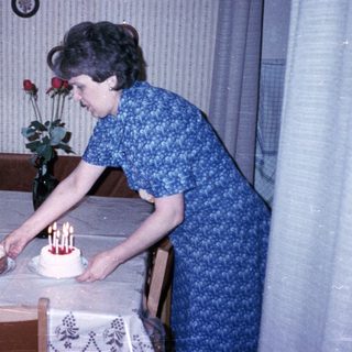 A woman lighting candles on two birthday cakes with a young boy seated.