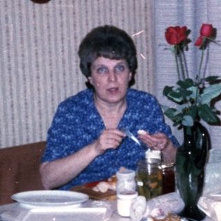 Woman sitting at kitchen table with flowers and food.