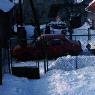 Snow-covered residential street with houses and parked cars.