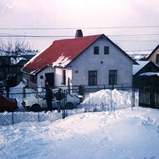 Snow-covered residential street with houses and parked cars.