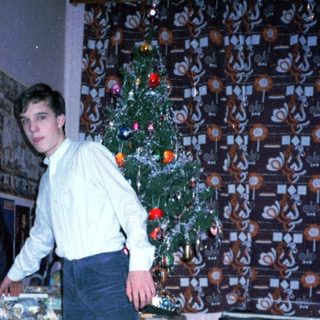 Young man standing by decorated Christmas tree in living room.