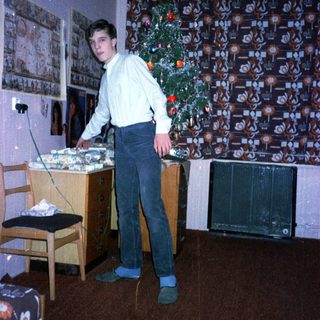 Young man standing by decorated Christmas tree in living room.