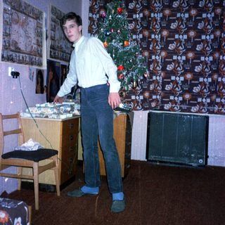 Young man standing by decorated Christmas tree in living room.