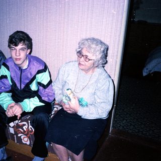 Family trio sitting indoors, dressed in 1980s-90s attire.