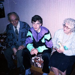 Family trio sitting indoors, dressed in 1980s-90s attire.
