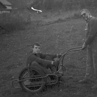 Two men in grassy field with manual wheelchair.