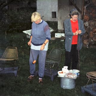 Two people preparing food outdoors during evening.