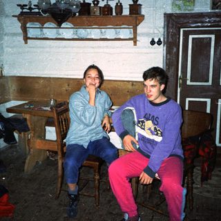 Two people sitting indoors, smiling in a rustic kitchen.