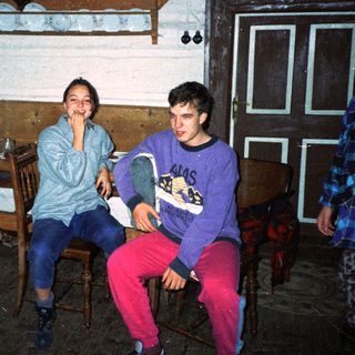 Two people sitting indoors, smiling in a rustic kitchen.